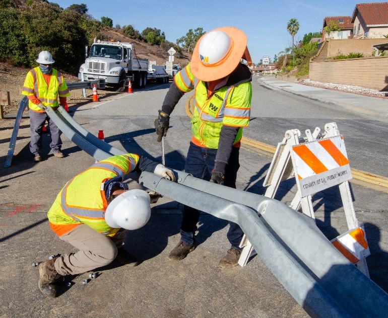 A group of Public Works’ construction workers repairing a guardrail along a street